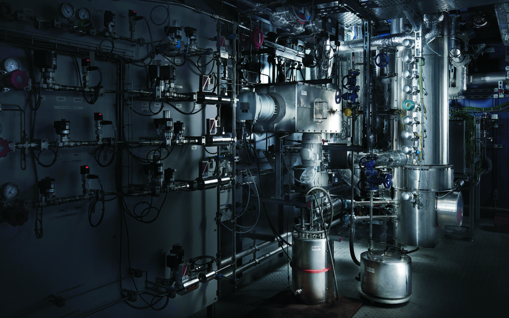 Säulenreaktor im Cointainer, der zur umweltfreundlichen Methanherstellung genutzt werden kann. Im Hintergrund befinden sich Leitungen. Das alles ermöglicht die Forschung für die Energiewende.