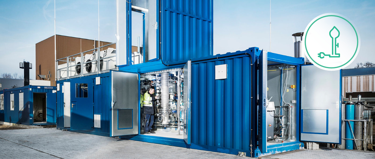 blauer zweistöckiger Containerbau mit geöffneten Türen. Einblick in die Methanisierungsanlage durch die Türen.